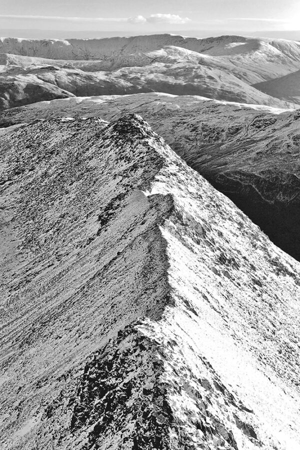 A black and white Lake District photograph by Jon Allison. The popular ridge of Striding Edge on Helvellyn, covered in snow in the glory of winter.