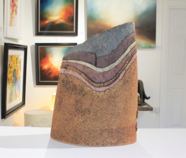 Landscape Vessel 14 by Cumbrian sculptural artist Nigel Edmondson. Hand-built using techniques in slab construction, coiling, throwing and often both in combination. Each piece is fired to a temperature of 1250C in oxidation, ensuring his creations can endure all weathers for the years to come. Landscape Vessel 14 is a 12” vessel made using clay. The layers of the clay are reminiscent of the fells of the Lake District, each with a different rusted earth tone in colour.