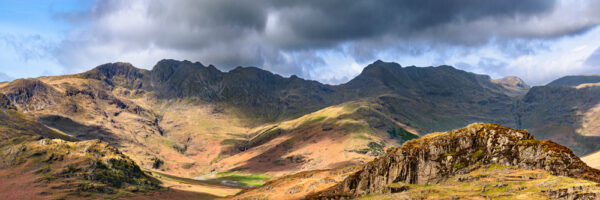 moody skies over the summits of bowfell and crinkle crags with harsh sunlight lake district photography by jon allison