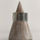 A chunky silver ring with a printed raindrop pattern along the band. Approximately 0.73” in diameter. Displayed on a wooden ring stand.