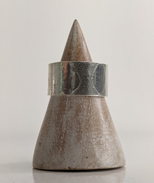 A chunky silver ring with a printed raindrop pattern along the band. Approximately 0.73” in diameter. Displayed on a wooden ring stand.