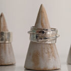 A chunky silver ring with a thin band detail layered over a hammered surface. Approximately 0.75” in diameter. Displayed on a wooden ring stand.