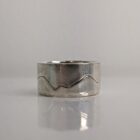 A chunky silver ring featuring a mountain range silhouette wrapping around its band and a hammered texture edge. Approximately 0.75” in diameter. This piece is on display at Cook House Crafts, Bowness-on-Windermere.