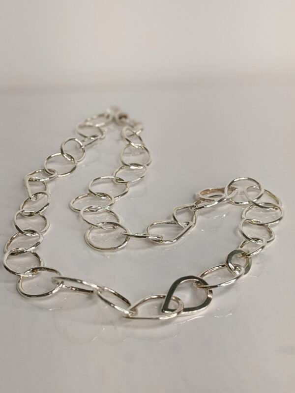 A handcrafted silver chain featuring a flowing arrangement of oval and raindrop shaped motifs. Chain is approximately 8“ in length.