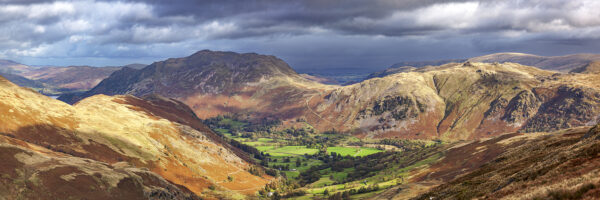 A view of Place Fell and Angletarn Pikes by Ullswater and Deepdale valley with strong sunlight and a moody sky in the background
