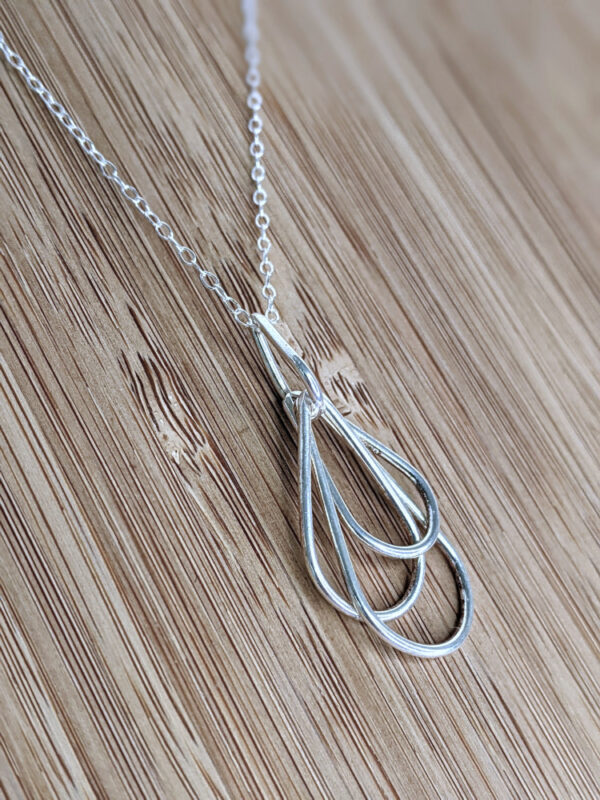 A handcrafted silver necklace showcasing four intertwined raindrop pendants. Chain is approximately 9“in length. Raindrop pendants approximately 1.75”.