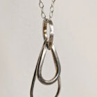 A handcrafted silver necklace showcasing three intertwined raindrop pendants. Chain is approximately 9“in length. Raindrop pendants approximately 1”. Close up image.