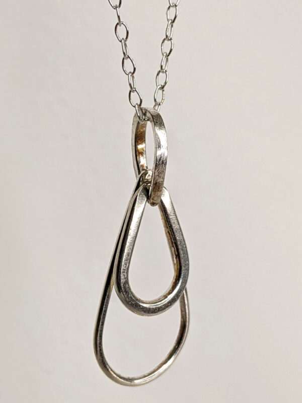 A handcrafted silver necklace showcasing three intertwined raindrop pendants. Chain is approximately 9“in length. Raindrop pendants approximately 1”. Close up image.