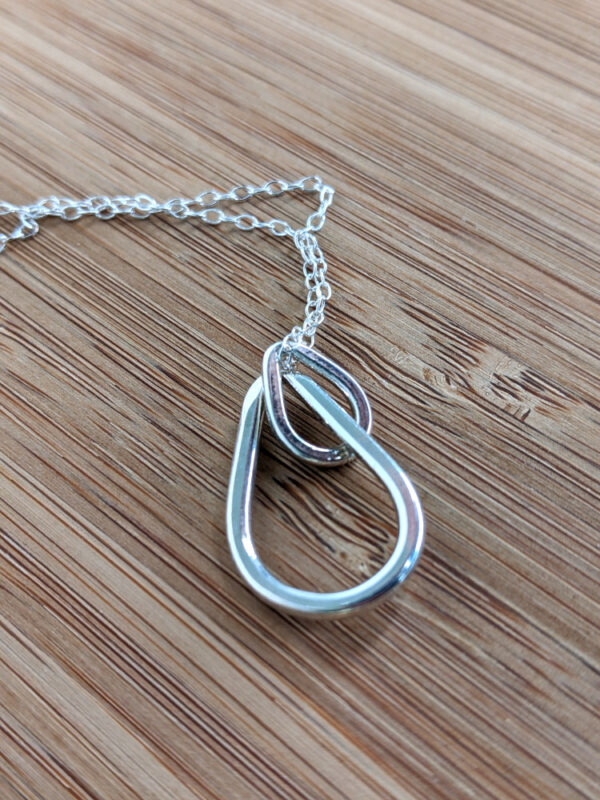 A handcrafted silver necklace showcasing two interlinked raindrop pendants. Chain is approximately 9“in length. Raindrop pendants approximately 1.25”.