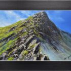 Lake District art original oil painting by Ben Goymour of a peak of a mountain central in the composition and blue skies. Displayed in a black frame with silver edge.