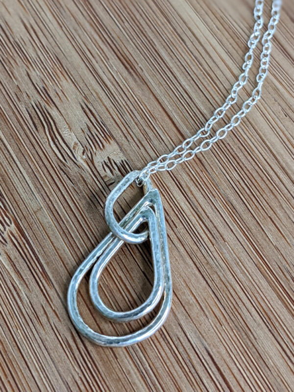 A handcrafted silver necklace showcasing three raindrop pendants with a hammered texture. Chain is approximately 9“in length. Raindrop pendants approximately 1.25”.