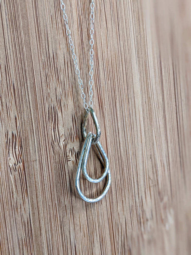 A handcrafted silver necklace showcasing three raindrop pendants with a hammered texture. Chain is approximately 9“in length. Raindrop pendants approximately 1.25”.