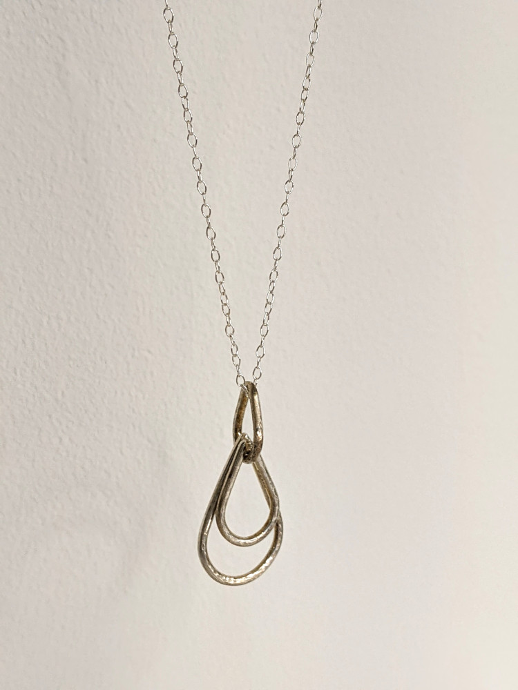 A handcrafted silver necklace showcasing three raindrop pendants with a hammered texture. Chain is approximately 9“in length. Raindrop pendants approximately 1.25”. White background.