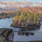 Lake District art original oil painting Tarn Hows by Simon Whitfield of the tarn with wooded island and sunlight lighting up the mountains behind.