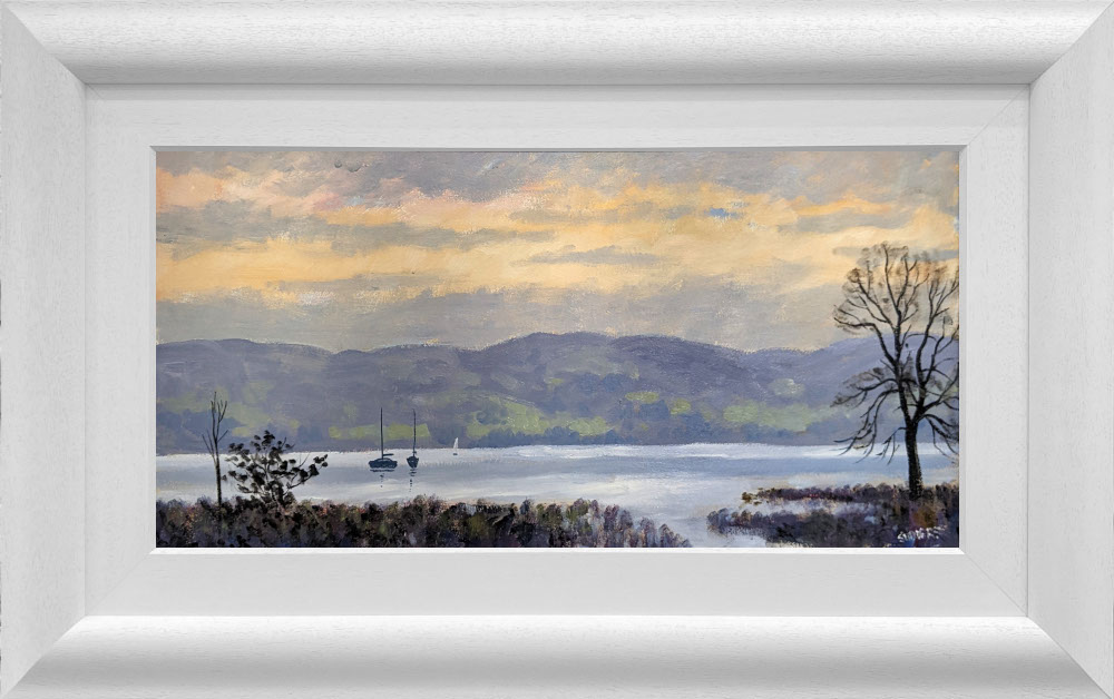 Lake District art original oil painting by Jeff Sudders. A clouded sunset and calm waters on Lake Windermere sailboat silhouettes in the distance. A calm piece. Displayed in a white cushioned frame.