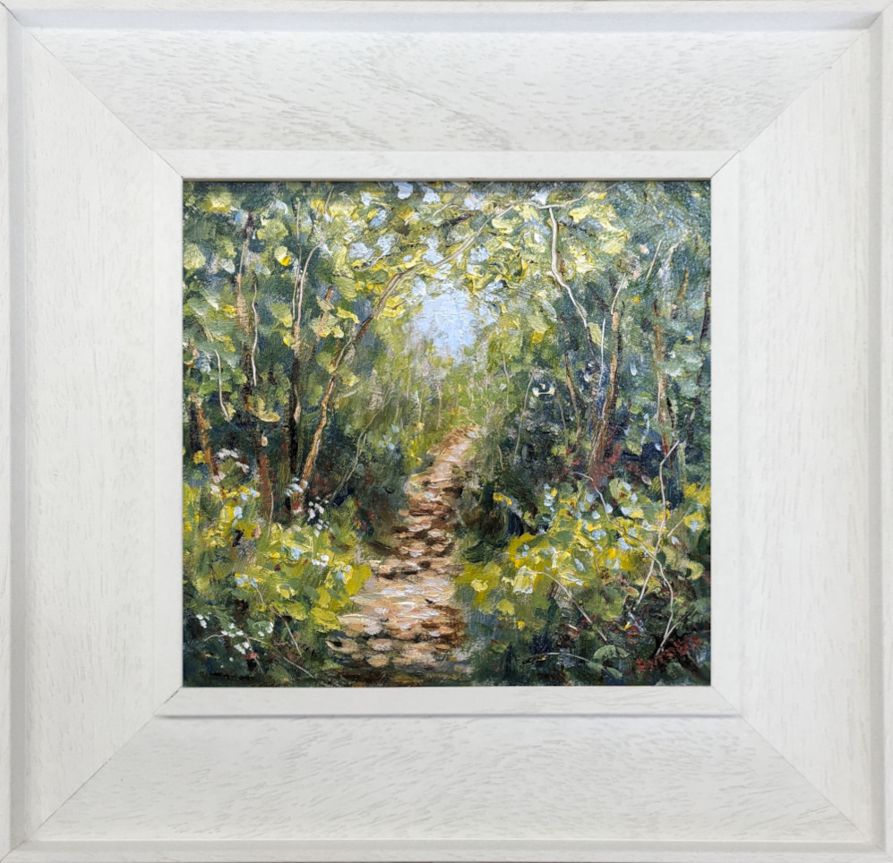 lake district art original oil painting by local artist Jeff Sudders. A woodland footpath with blossoming flowers blue skies peaking through the trees. Displayed in a white frame with wood grain.