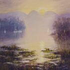 A misty sunrise over a calm lake with sailboats, distant mountains, and reeds in the foreground.