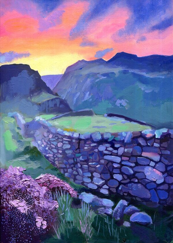 Colorful sunset over blue-green mountains, with a curved stone wall, grassy hillside, and pink wildflowers in the foreground.