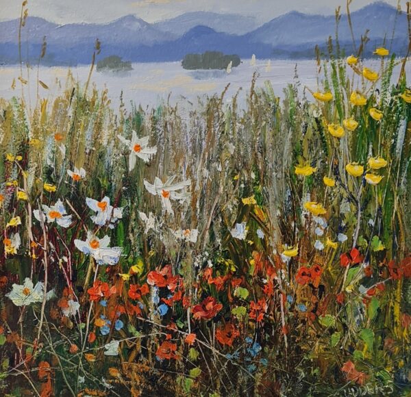 Wildflowers bloom along a lakeshore, with sailboats, wooded islands, and blue mountains in the distance.