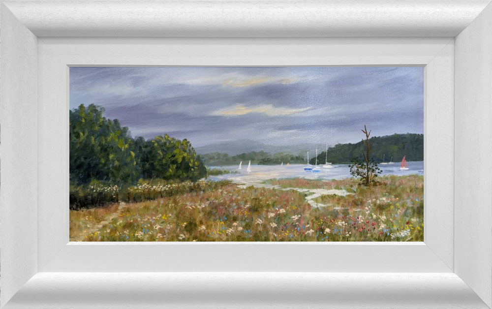 Lake District art original oil painting by Jeff Sudders. Summer Meadows by Windermere featuring sailboats floating on the lake moody grey skies and a meadow of flowers in the foreground. Displayed in a white cushioned frame.